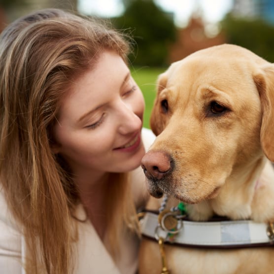 A woman smiling looking at her yellow Labrador Guide Dog