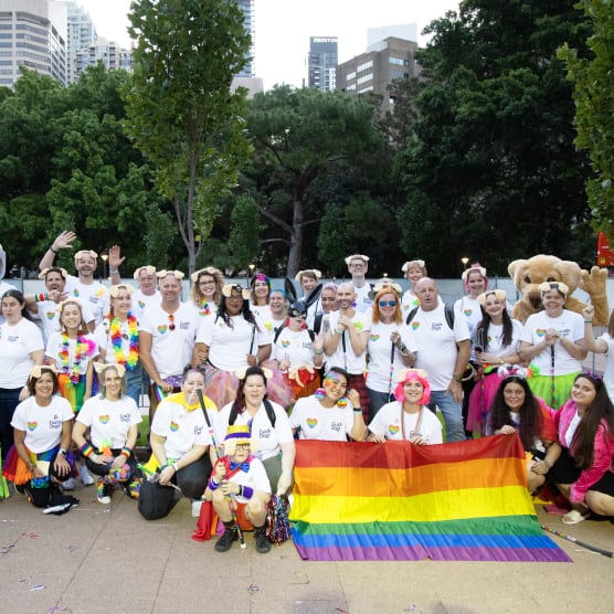 A group of people wearing dog ears facing the camera with a rainbow flag