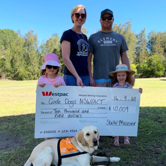 Stella and her family holding a giant cheque for $10,009 with a yellow Labrador lying in front of them.
