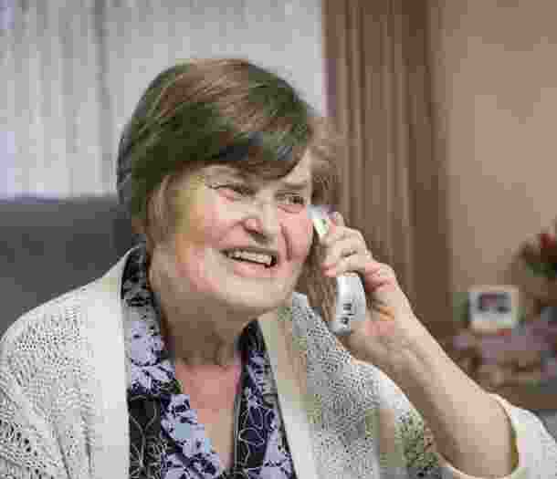 An older adult sitting on a couch on her phone with a smile of their face.