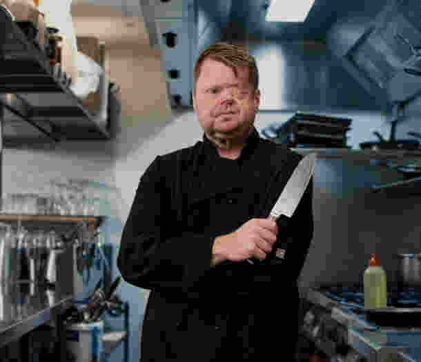 Craig stands in a commercial kitchen holding a large chef's knife.